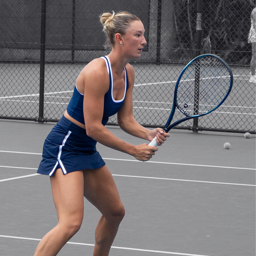 Tennis player in blue Rallee Cross court active top, holding a racket on a court
