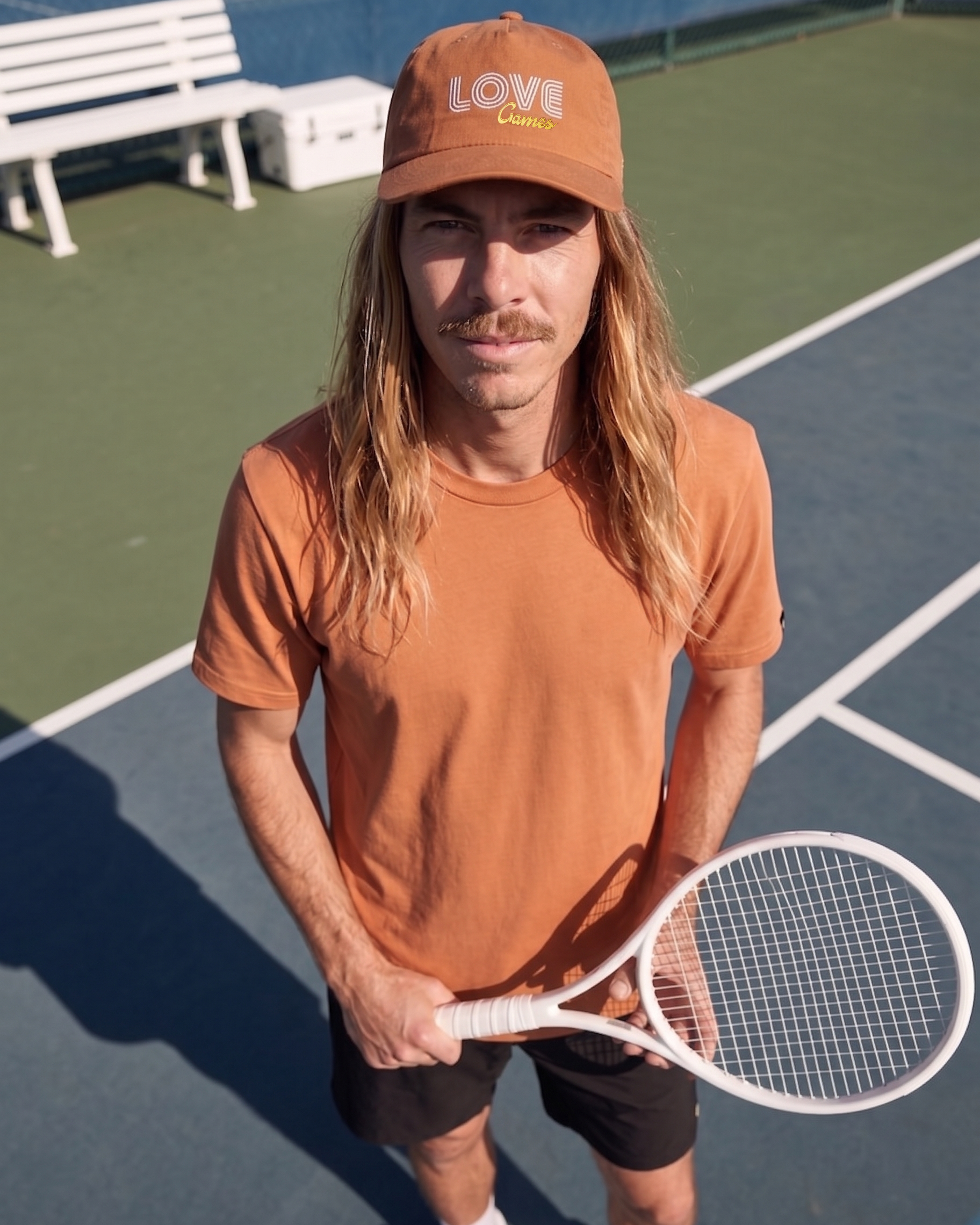 Person wearing an clay coloured cap and shirt holding on a tennis court