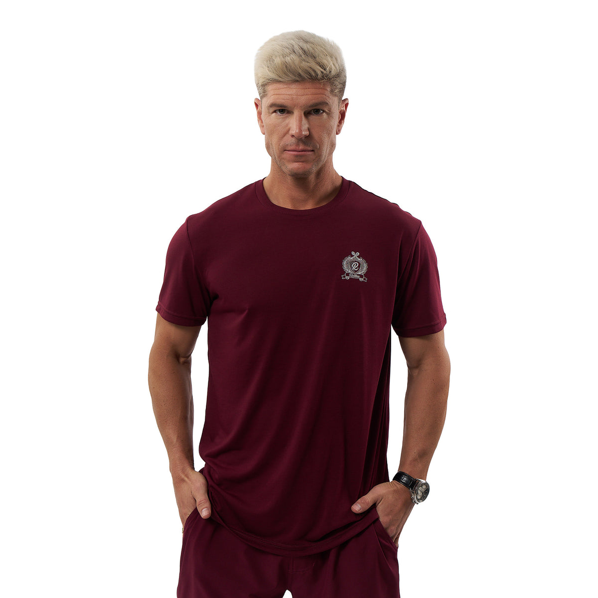 A man with short blonde hair wearing a maroon short-sleeve athletic t-shirt and matching maroon shorts, standing against a plain white background.