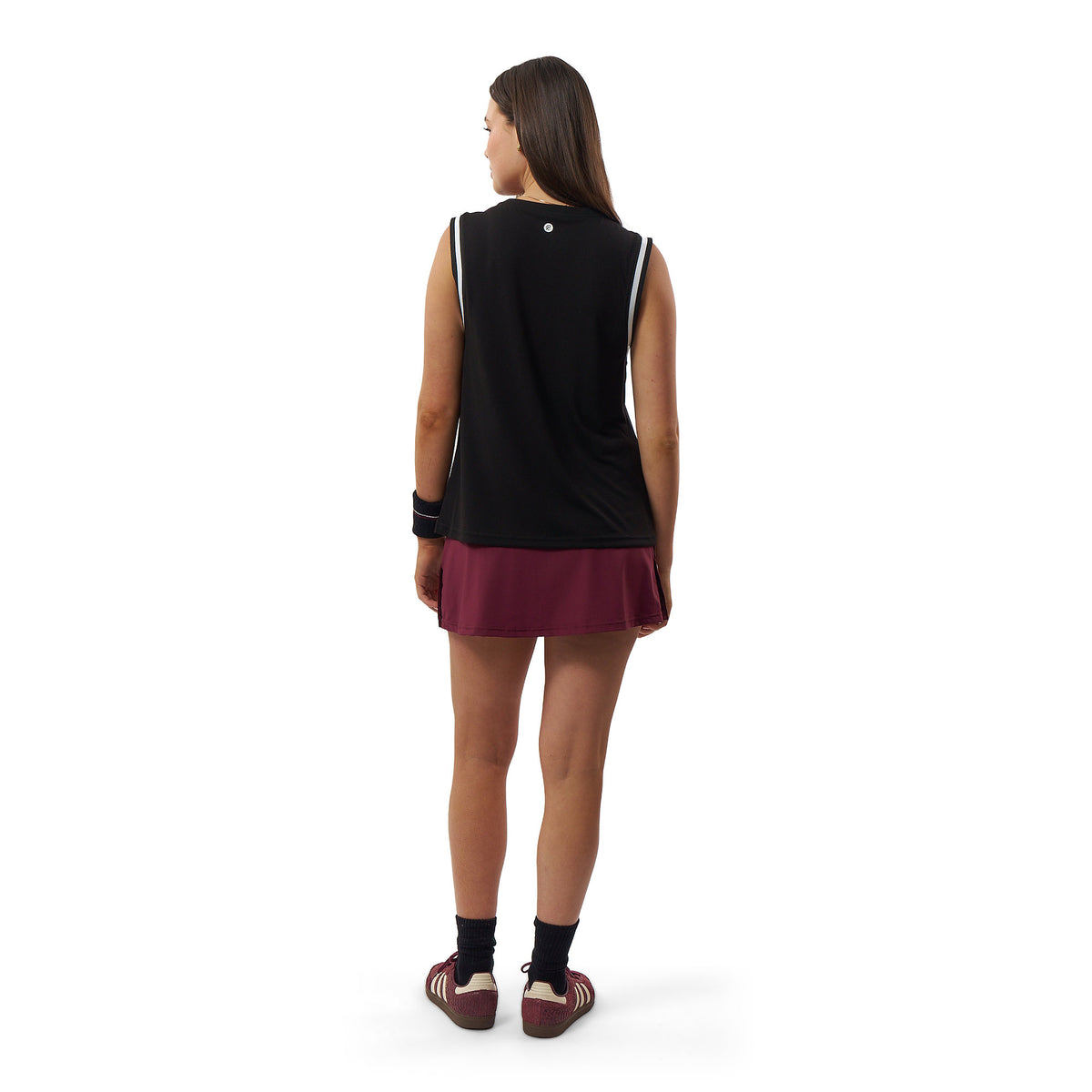 A woman is shown from behind wearing a sleeveless black athletic top and a maroon mini skirt, paired with black socks and maroon sneakers, against a plain white background.