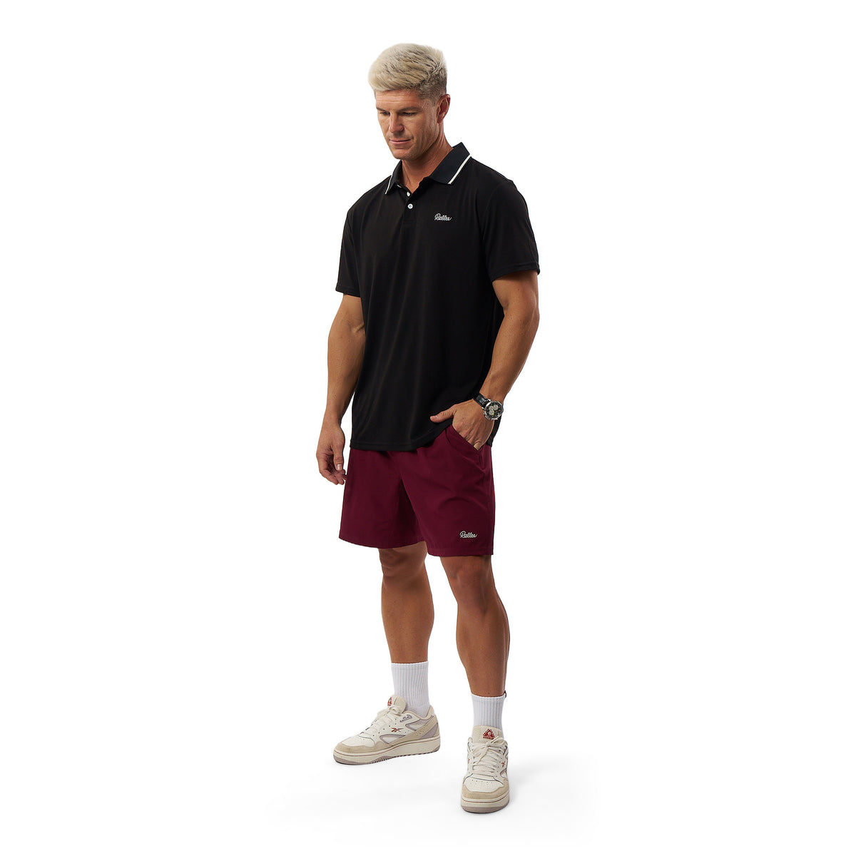 A man modeling a black short-sleeve polo shirt and burgundy athletic shorts against a plain white background.