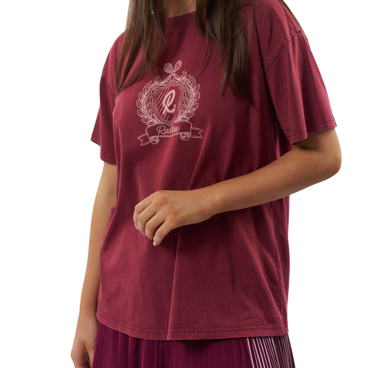 A woman wearing a faded burgundy short-sleeve t-shirt with a white graphic print on the chest featuring a monogram 'R' in an ornate crest and the word 'Rallee'.