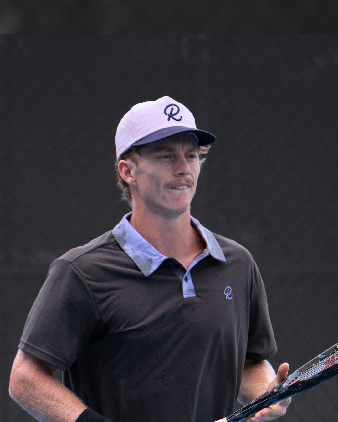 Man wearing a cap and holding a tennis racket against a dark background