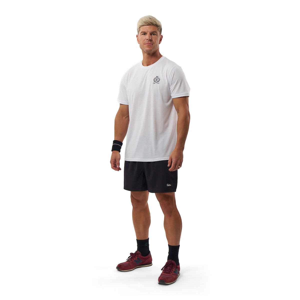 A man modeling a white short-sleeve athletic t-shirt with a small gray chest logo, paired with black athletic shorts, black socks, and burgundy athletic shoes, against a plain white background.