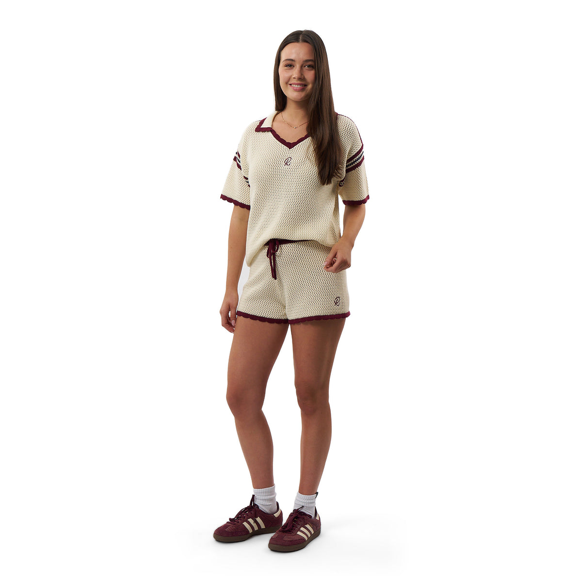 A woman modeling a cream-colored mesh athletic set consisting of a short-sleeve V-neck jersey and matching shorts, accented with dark red trim and white socks, against a plain white background.