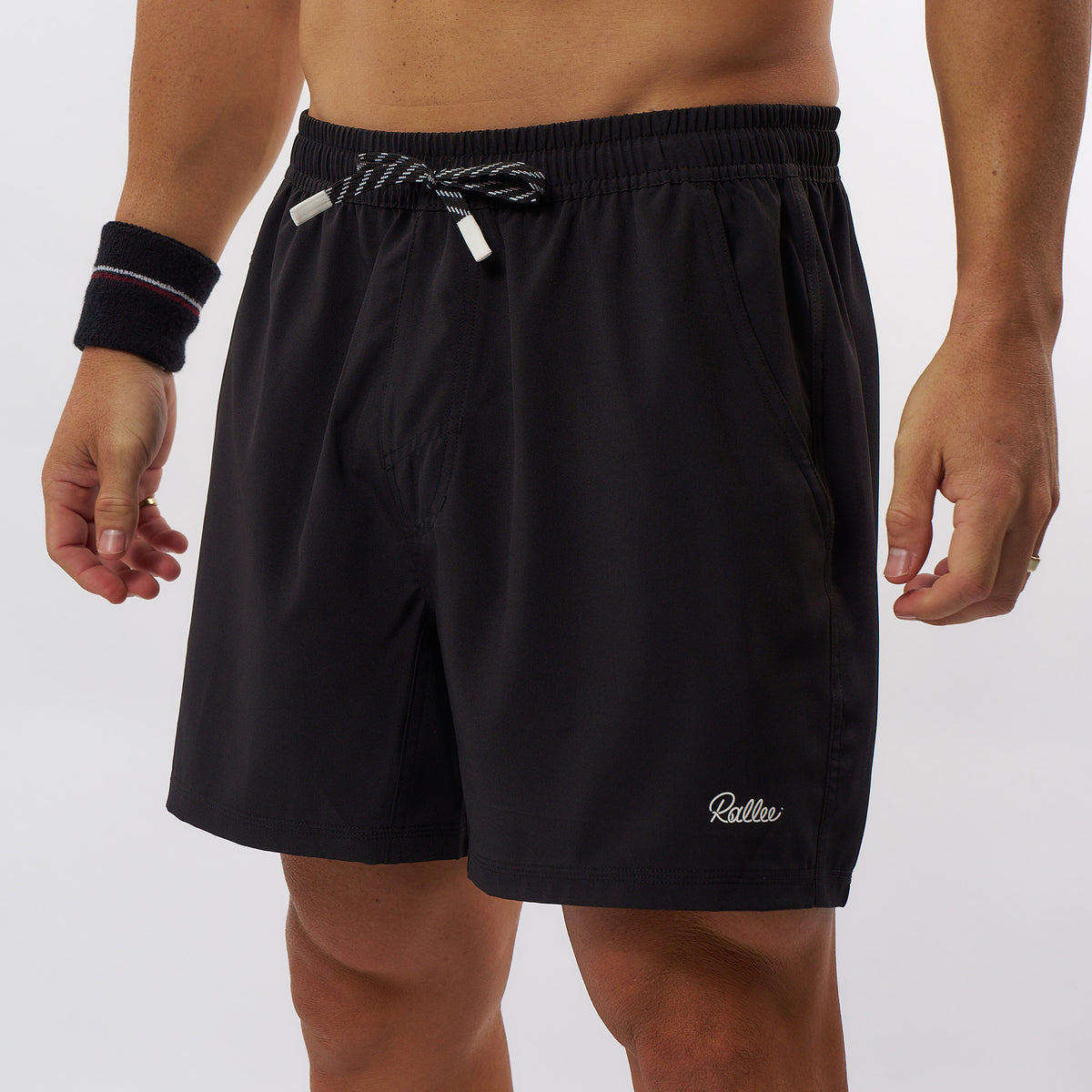 Black athletic tennis shorts with a white embroidered 'Bellerose' logo on the lower left leg, featuring a black elastic waistband with a white and black striped drawstring, shown on a model.