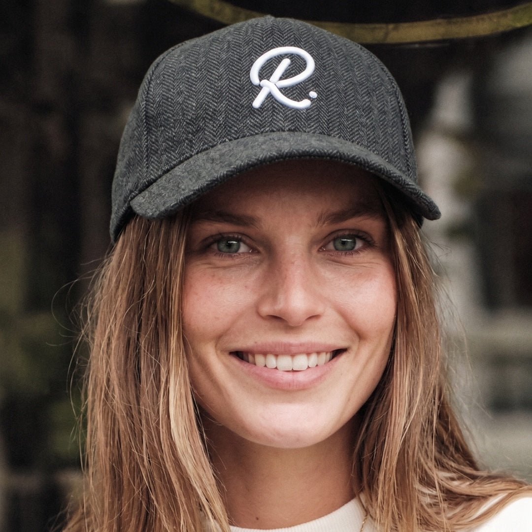 Woman wearing a gray cap with a white logo, smiling outdoors.
