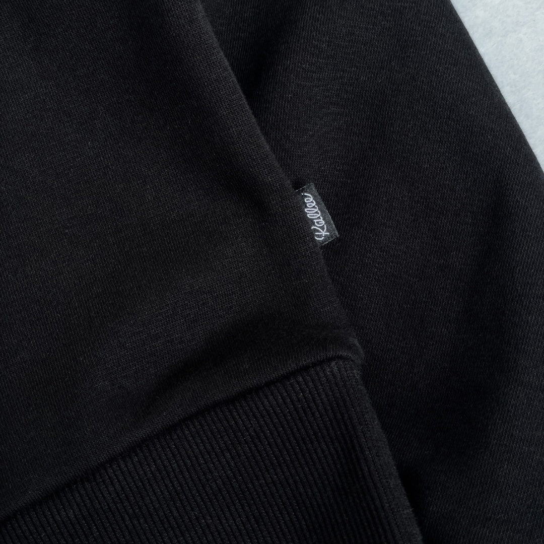 Close-up of a black hoodie with a brand label on a light gray background