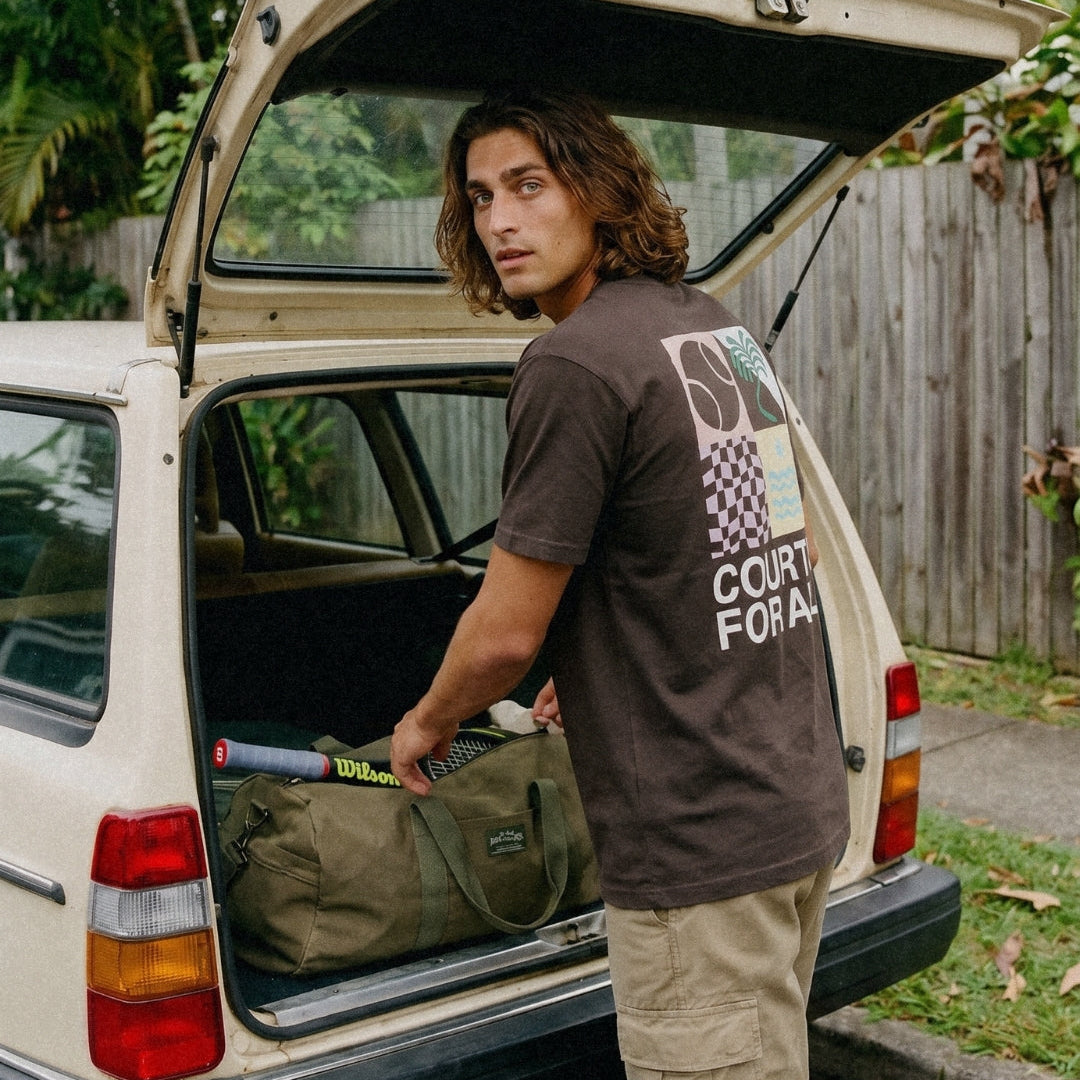Man loading a duffel bag into the back of a van with a scenic outdoor background