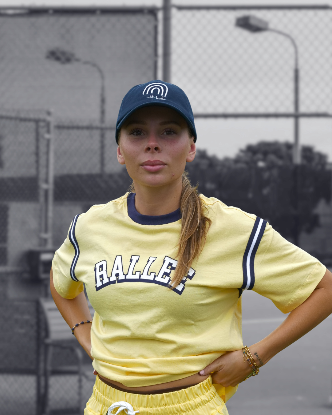 Person wearing a yellow 'RALLEE' jersey and blue cap on a tennis court