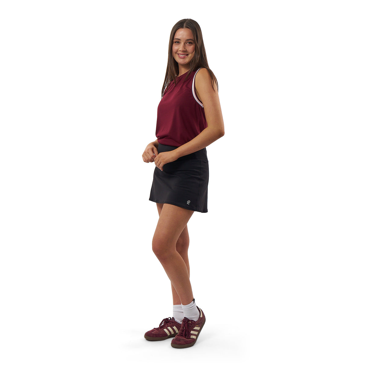 A woman modeling a sleeveless maroon athletic top and a black tennis skirt against a plain white background.