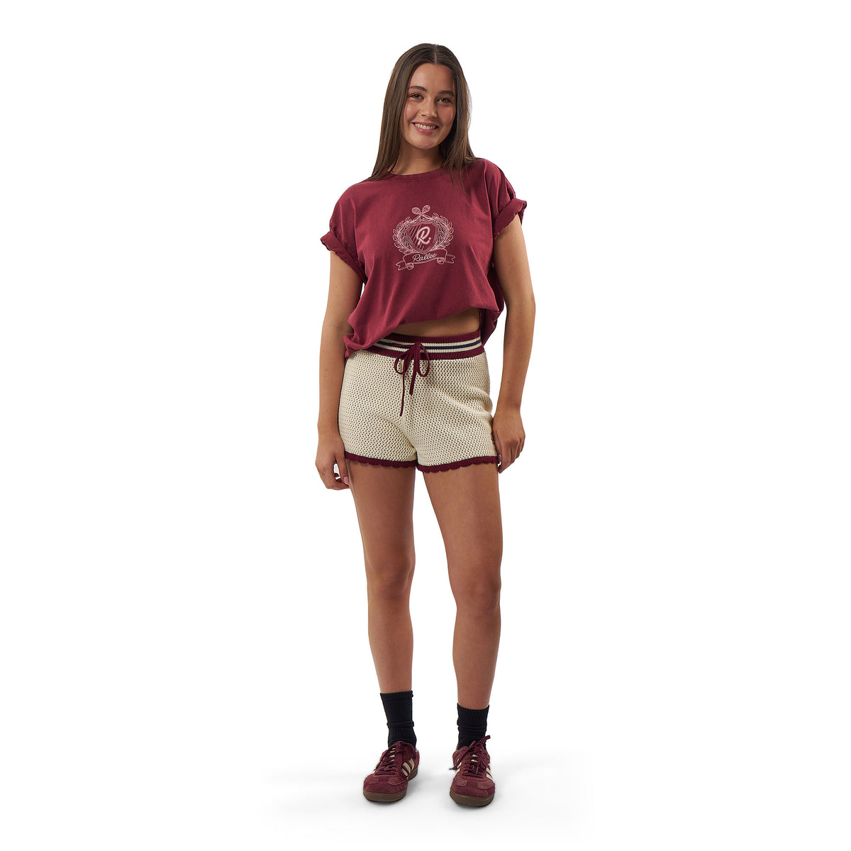 A young woman modeling a matching athletic lounge set consisting of a short-sleeve cropped t-shirt and drawstring shorts in maroon and cream mesh.