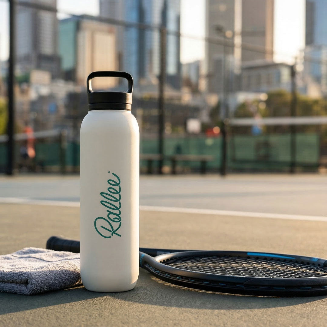 White waterdro® bottle with 'Rallee' branding on a tennis court with city skyline in the background