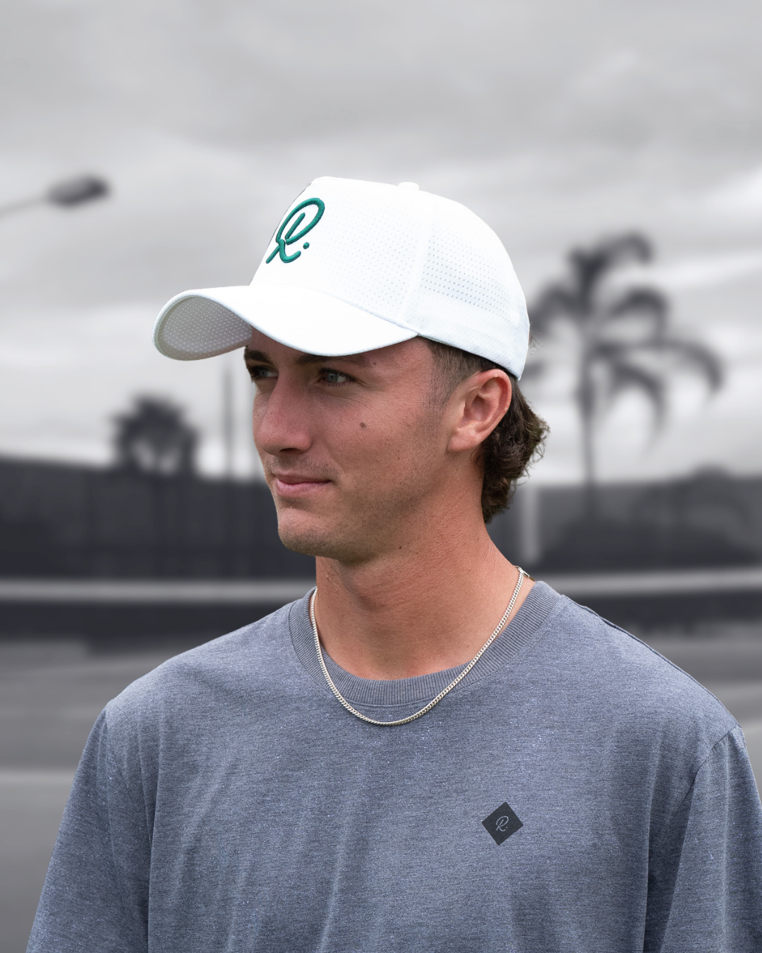 Man wearing a white cap with 'R' logo and grey Rallee shirt outdoors