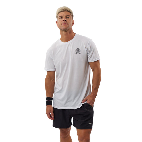 A man modeling a white short-sleeve athletic t-shirt with a small black chest logo, paired with black athletic shorts, against a solid white background.