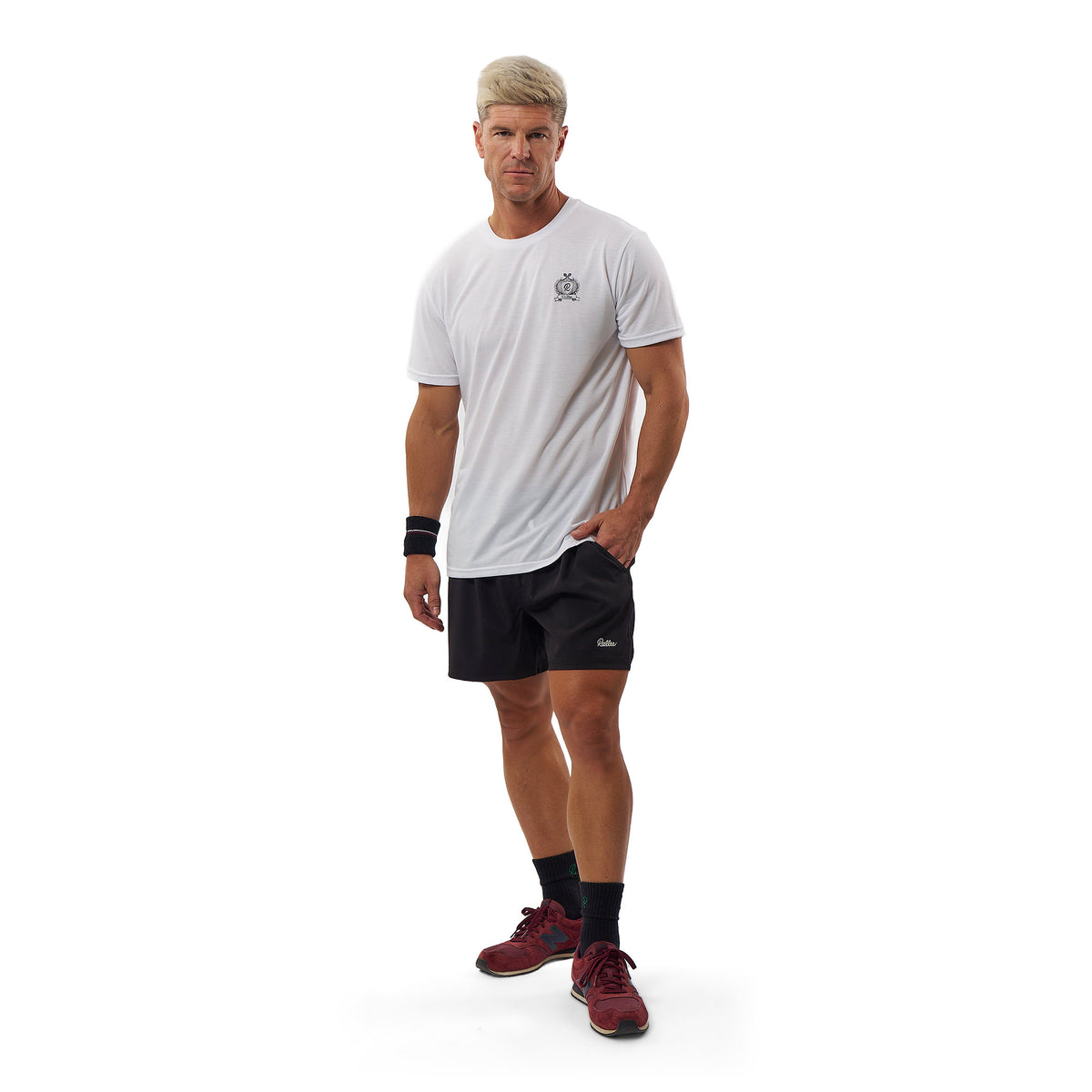 A man modeling a white short-sleeve athletic t-shirt with a small gray logo on the left chest, paired with black athletic shorts, black socks, and burgundy athletic shoes, against a solid white background.