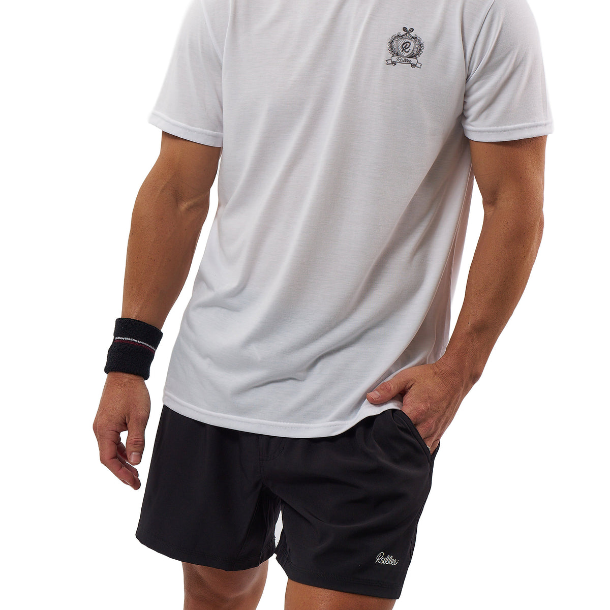A man wearing a white short-sleeve athletic t-shirt with a small crest logo on the left chest and black athletic shorts with a small white script logo near the hem. He is also wearing a black wristband, photographed against a plain white background.