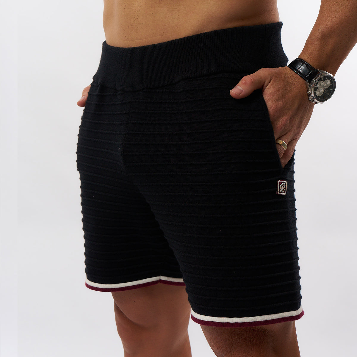 Black ribbed athletic shorts with a white and burgundy hem trim, shown on a model against a light gray background.