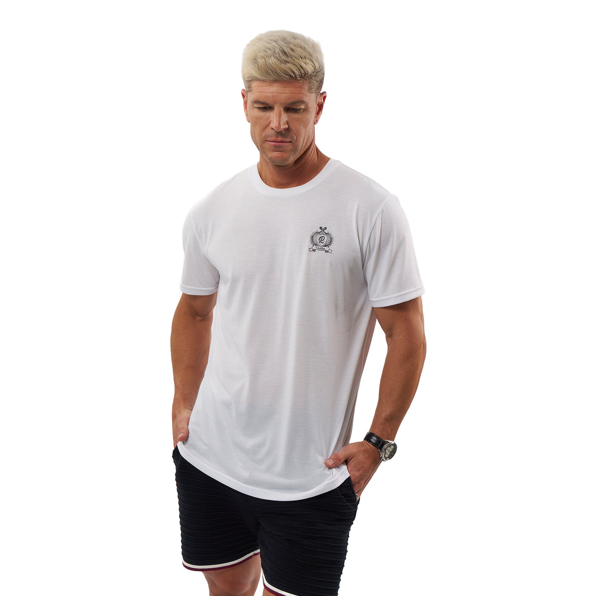 A man wearing a white short-sleeve crewneck t-shirt with a small black crest logo on the left chest, paired with black athletic shorts, against a solid white background.