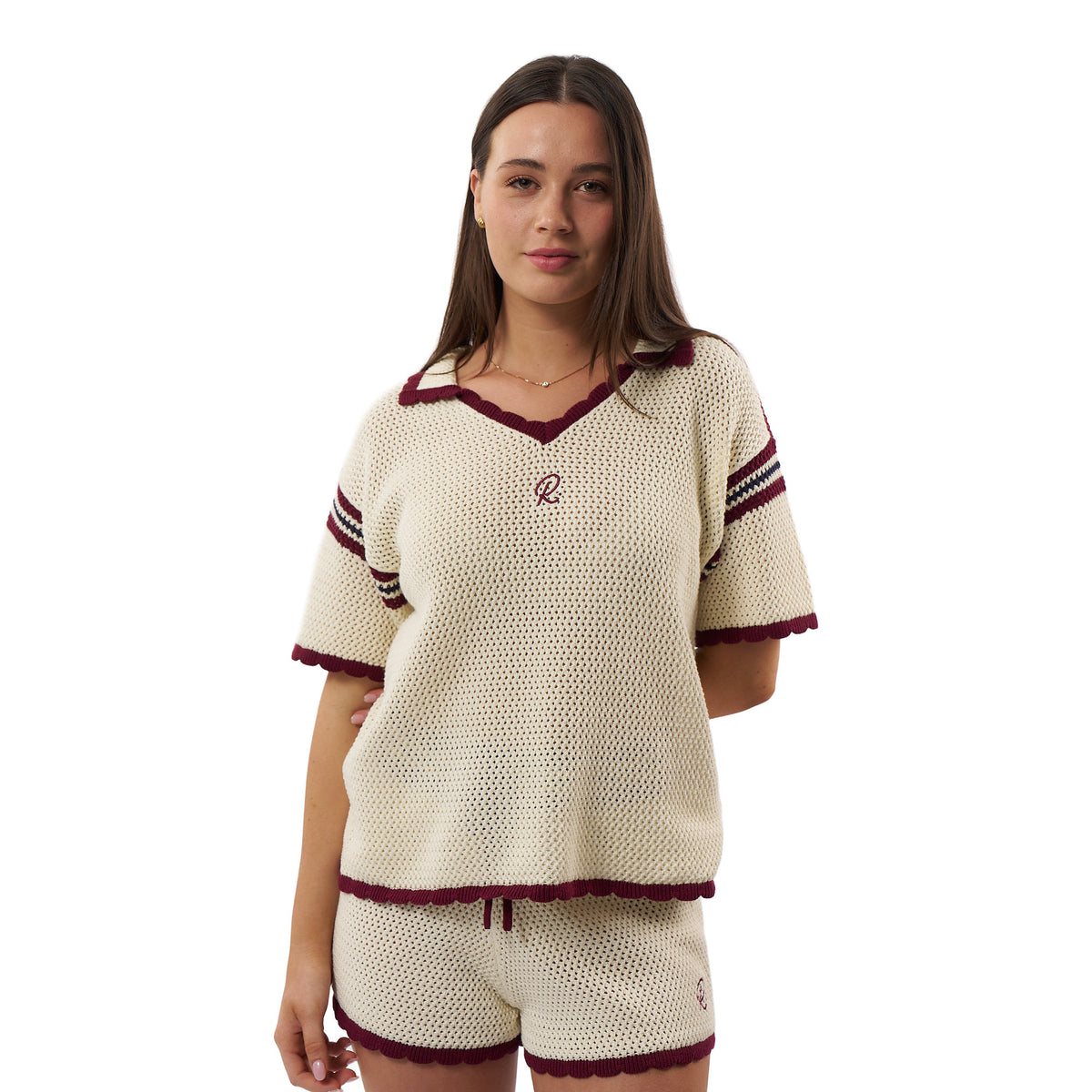 A woman modeling a matching knit lounge set consisting of a short-sleeve V-neck top and shorts in cream with burgundy trim and sleeve stripes, on a plain white background.