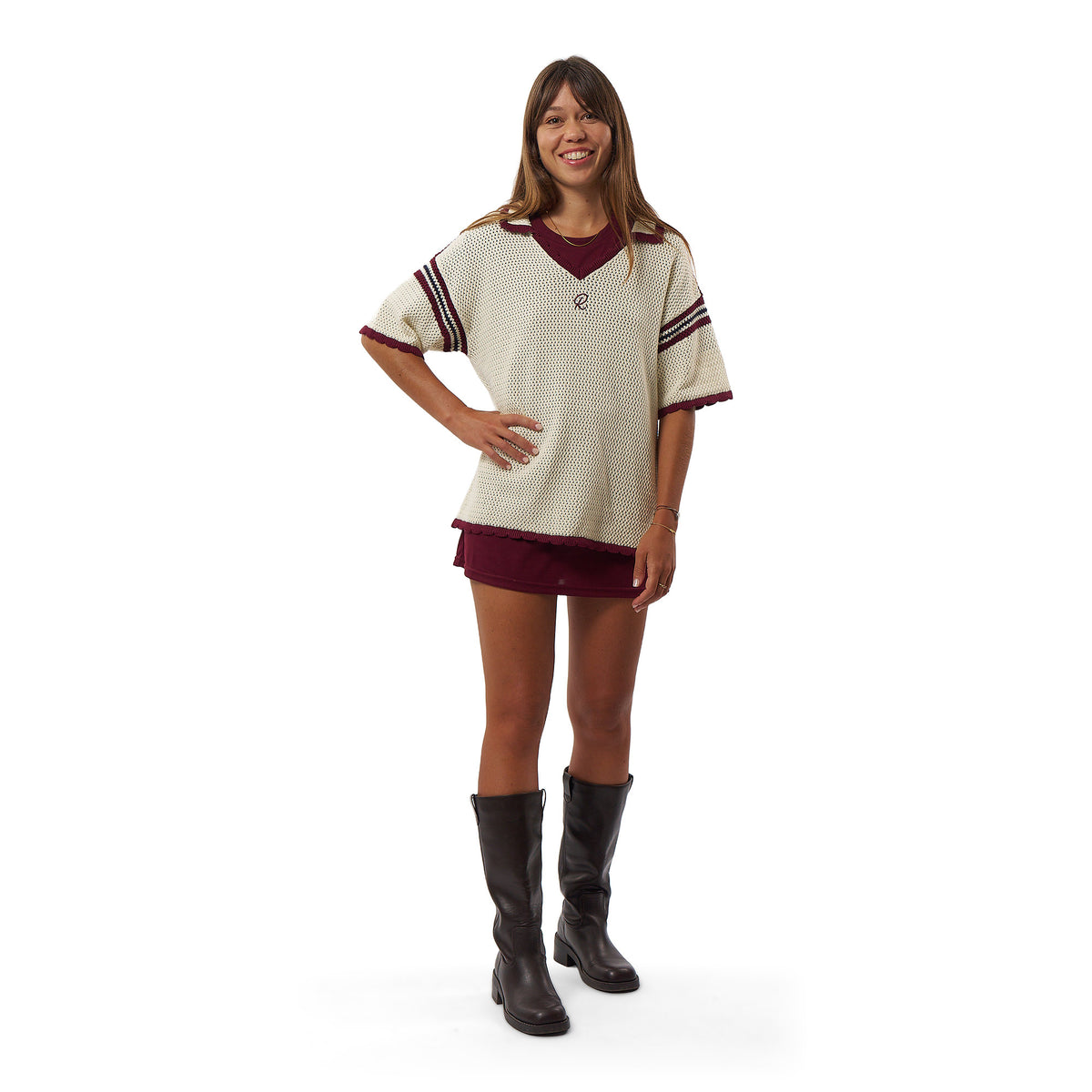 A woman modeling a vintage-style knit v-neck sweater in cream with maroon trim and a maroon mini skirt, paired with black knee-high boots, against a plain white background.