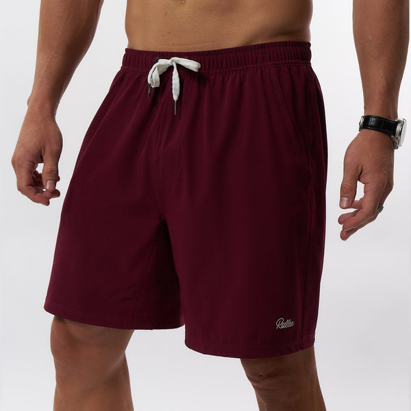 A man wearing burgundy athletic shorts with a white drawstring and a small white script Rallee logo on the lower left leg, shown against a light gray studio background.